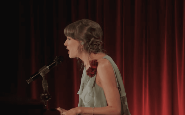 Taylor Swift wears a green dress with floral details and wears her hair in a low updo.